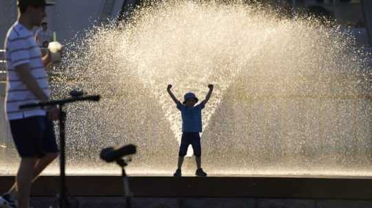 Chlapec sa hrá vo fontáne počas horúčav.