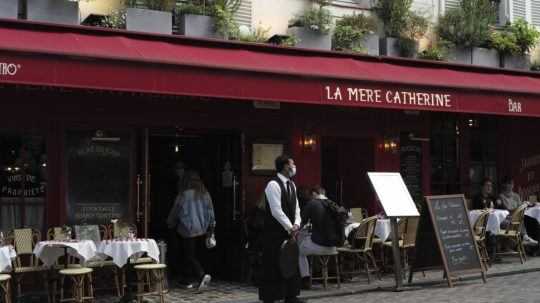 Čašník stojí pred reštauráciou na letnej terase po jej znovuotvorení po lockdowne v štvrti Montmartre v Paríži 19. mája 2021.
