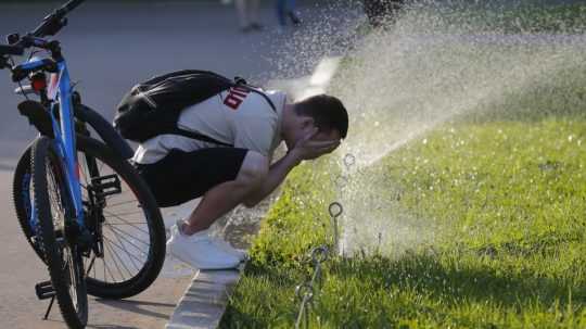 Muž sa osviežuje vodou určenou na zavlažovanie trávnika.