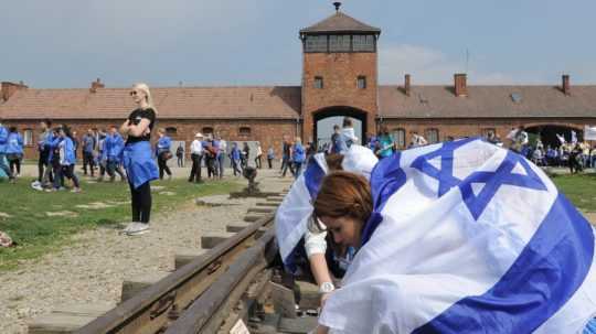 Dievča kladie spomienkovú tabuľu na koľajnice v Auschwitzi.