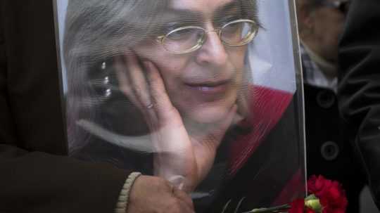 Žena drží kvety a portrét zavraždenej novinárky Anny Politkovskej.