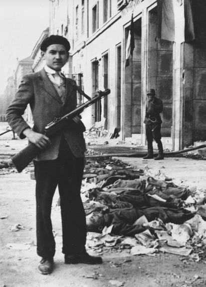 Mladý maďarský revolucionár stojí s automatickou zbraňou pri rade mŕtvych sovietskych vojakov.