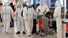 Pasažieri na letisku v Sydney oblečení v ochranných oblekoch.