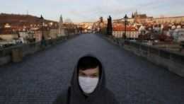 Na archívnej snímke zo 16. marca 2020 mladý muž s ochranným rúškom kráča po Karlovom moste v Prahe.