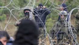 Poľskí policajti a príslušníci pohraničnej stráže hliadkujú pri plote s ostnatým drôtom.