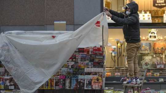 Predavač zakrýva novinový stánok plastovou prikrývkou na obchodnej ulici vo Viedni.