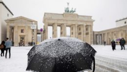 Muž stojí s dáždnikom v snehu pred Brandenburskou bránou v Berlíne.