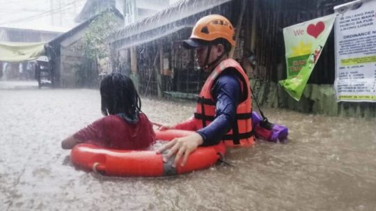 Záchranár pomáha dievčaťu, ktoré sa brodí po zaplavenej ulici počas vyčíňania tajfúnu Rai.