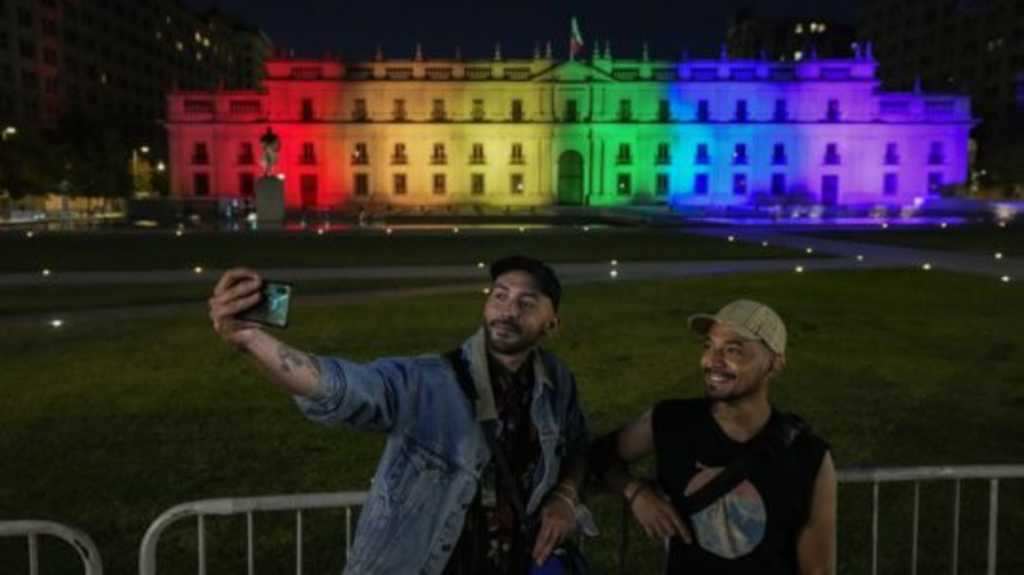 Homosexuálny pár sa fotí pred prezidentským palácom v čilskom Santiagu vysvieteným vo farbách dúhy.
