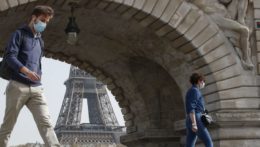 Ľudia s ochrannými rúškami kráčajú cez most Bir-Hakeim v Paríži, v pozadí Eiffelova veža.