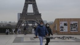 Ľudia s ochrannými rúškami kráčajú cez námestie Trocadero Plaza v Paríži.