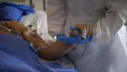 Lekár v špeciálnom ochrannom odeve drží ruku pacienta s ochorením COVID-19.
