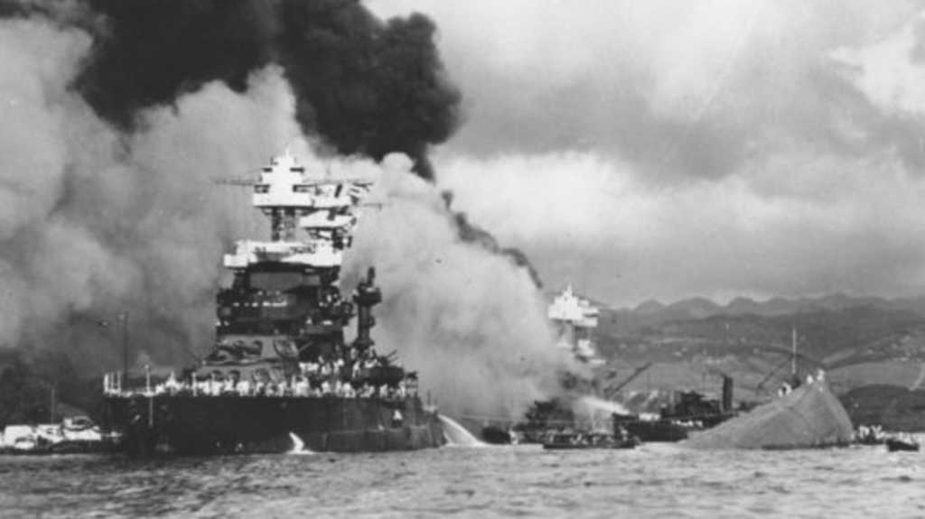 Na archívnej snímke vpravo časť trupu potápajúcej sa bojovej lode USS Oklahoma, uprostred potápajúca sa bojová loď USS West Virginia a vľavo loď USS Maryland je stále na hladine počas japonského útoku na Pearl Harbor.