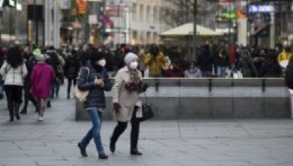 Ľudia s ochrannými rúškami kráčajú na obchodnej ulici vo Viedni.