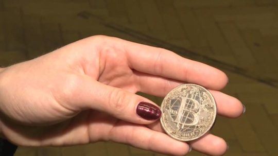 Žena drží v ruke mincu bitcoinu.