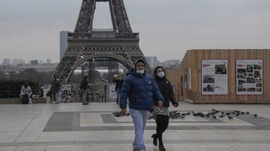 Ľudia s ochrannými rúškami kráčajú cez námestie v Paríži.