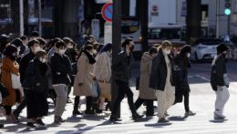 Ľudia s ochrannými rúškami kráčajú cez križovatku v Tokiu.