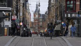 Ľudia kráčajú poloprázdnou ulicou v centre Amsterdamu.