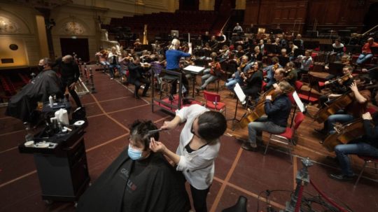Kaderníci strihajú zákazníkov na pódiu počas skúšky Kráľovského orchestra Concertgebouw v Amsterdame.