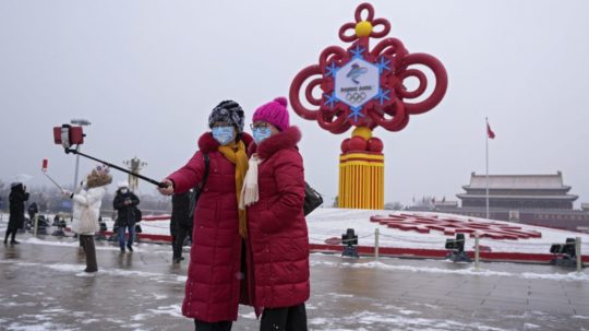 Ženy s ochrannými rúškami sa fotia pred dekoráciou na zimné olympijské hry v Pekingu.