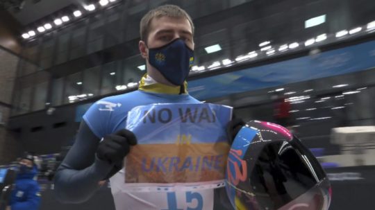 Na videosnímke ukrajinský skeletonista Vladyslav Heraskevyč ukazuje do kamier papier s nápisom "Nie vojne na Ukrajine".