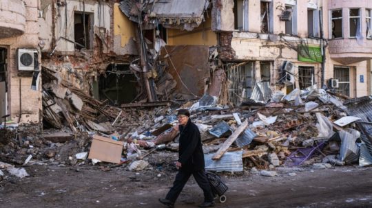 Starý muž kráča popri zničenej budove v ukrajinskom meste Charkov.