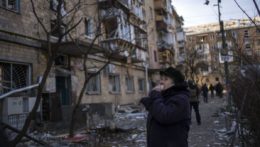 Žena v Kyjeve hľadí na zničenú obytnú budovu.