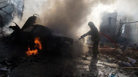 Na snímke hasič hasí horiace auto v kyjevskej štvrti zničenej po ruskom bombarodvaní