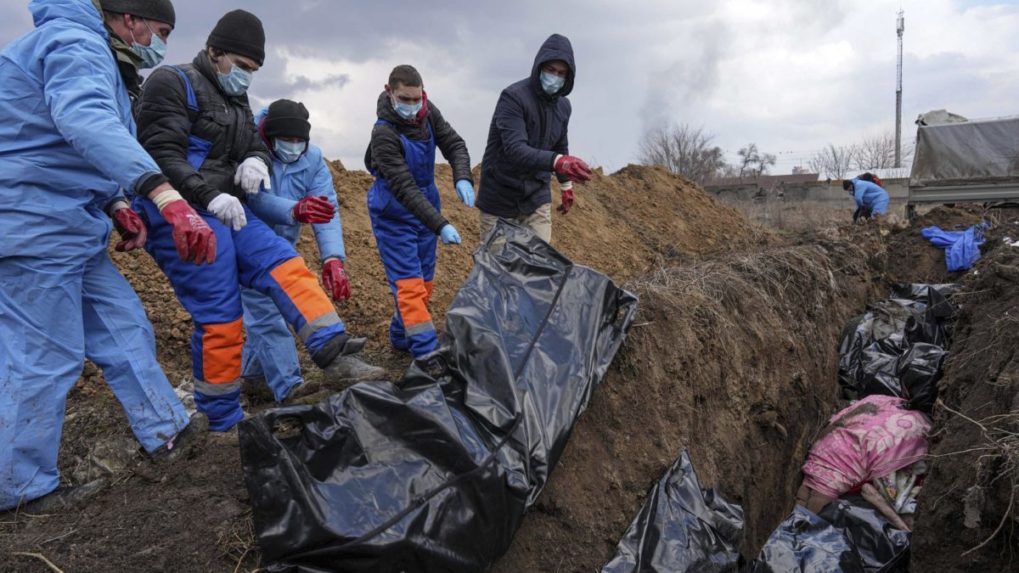 Ľudia hádžu zabalené mŕtve telá do masového hrobu v Mariupole.