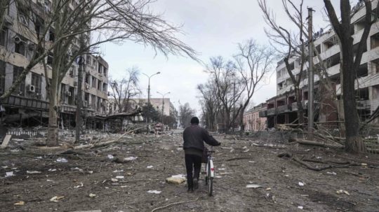 Muž s bicyklom sa prechádza ulicou Mariupolu po zničení ruským bombardovaním.