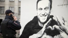 Policajt stojí pred grafiti zobrazujúcim väzneného ruského opozičníka Alexeja Navaľného.
