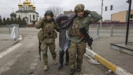 Ukrajinskí vojaci pomáhajú staršej žene v meste Irpiň.