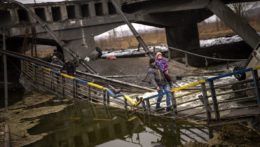 Miestny milicionár nesie dieťa, keď pomáha utekajúcej rodine cez most zničený delostrelectvom na predmestí Kyjeva na Ukrajine.