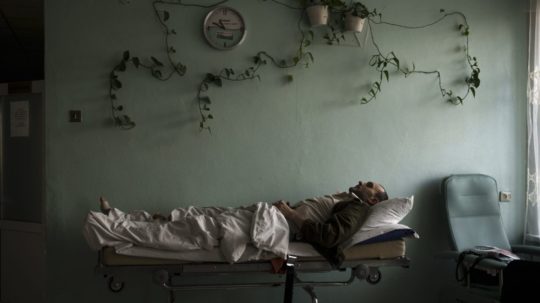 Muž leží na posteli na chodbe ukrajinskej nemocnice v Brovaroch.