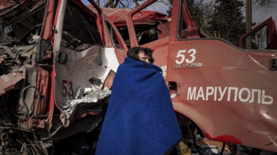 Žena s dekou stojí pri hasičskom aute v Mariupole po ruskom bombardovaní.