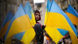 Ľudia mávajú s ukrajinskými vlajkami počas protestu proti ruskej invázii na Ukrajine.