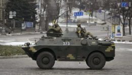 Ukrajinskí vojaci sedia na vrchu obrneného vozidla pri prechádzaní prázdnou ulicou počas poplachu leteckého útoku v Kyjeve.