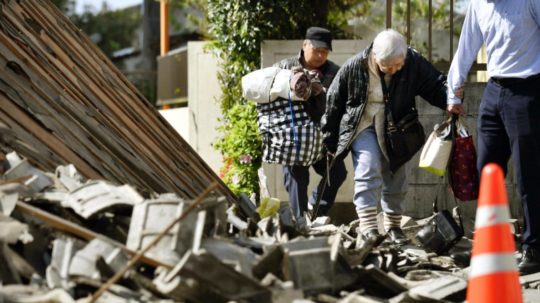 Obyvatelia kráčajú cez trosky zničených domov po zemetrasení v Japonsku.