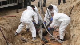 Muži v špeciálnych ochranných odevoch exhumujú telá civilistov z masového hrobu v ukrajinskom meste Buča.