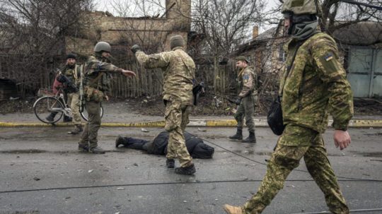 Ukrajinskí vojaci okolo tela mŕtveho civilistu v Buči.