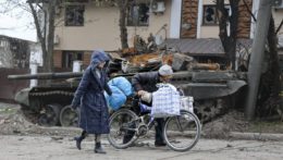 Na snímke miestni civilisti kráčajú okolo zničeného tanku počas bojov medzi ukrajinskou a ruskou armádou v obliehanom meste Mariupol.