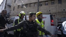 Izraelský pohraničný policajt stojí medzi sanitkou vezúcou zraneného muža a rozhnevaným davom.