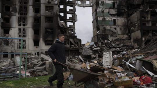 muž tlačí fúrik pred raketami zničenou bytovkou v ukrajinskej Boroďanke