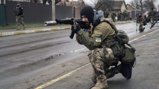 Ukrajinský vojak zabezpečuje presun spolubojovníkov počas kontroly nástražných pásc v meste Buča.