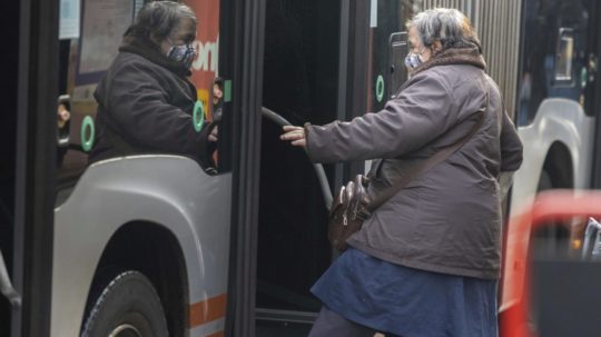 Žena s ochranným rúškom nastupuje do autobusu.