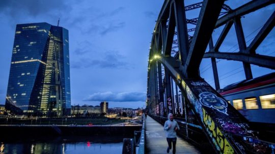 Muž behá cez most neďaleko budovy Európskej centrálnej banky vo Frankfurte nad Mohanom.