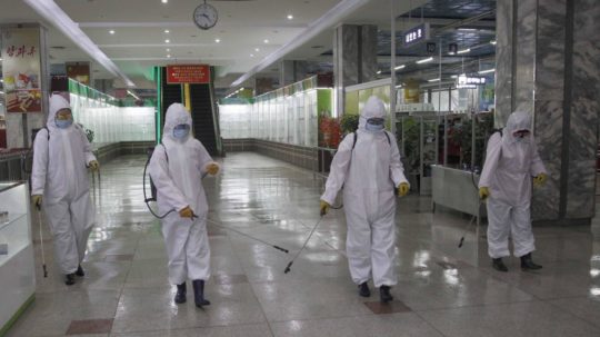 Zamestnanci v špeciálnych ochranných odevoch dezinfikujú priestory obchodu proti šíreniu ochorenia COVId-19 v Pchjongjangu.