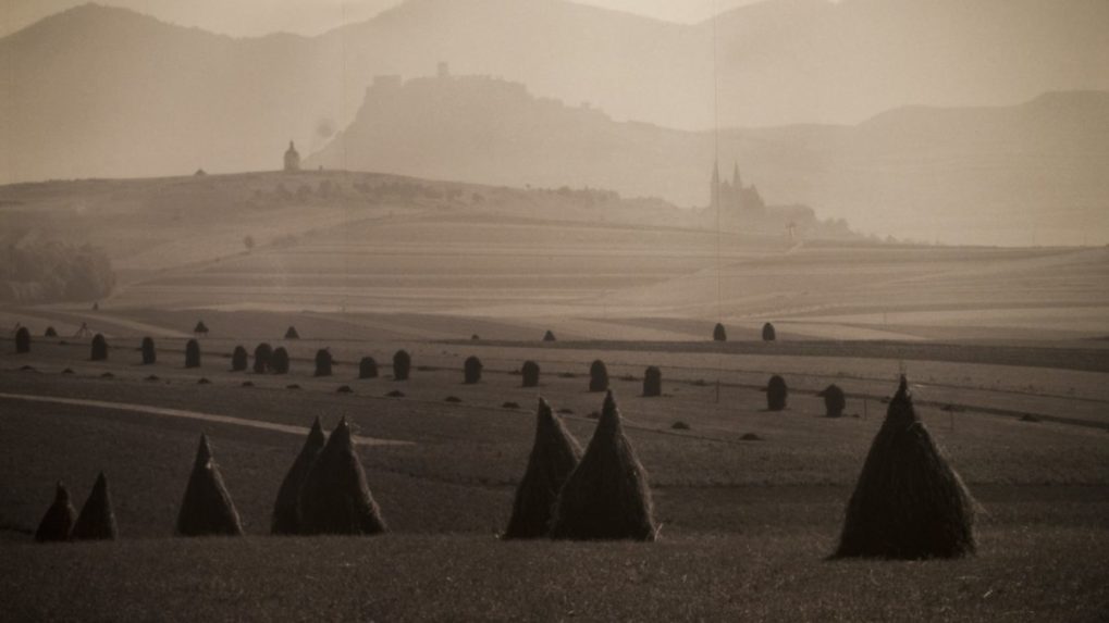 Na snímke fotografia Karola Plicku znázorňujúca pole s kopami sena pod Spišským hradom.