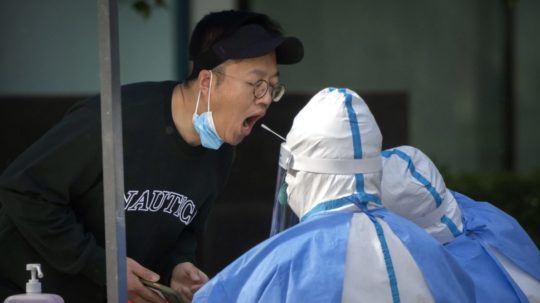 Zdravotník v ochrannom odeve odoberá vzorku obyvateľovi počas tretieho dňa masového testovania na ochorenie COVID-19 pred komerčnou budovou v čínskom Pekingu.
