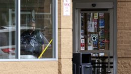 Policajt sa pozerá cez okno v obchode, v ktorom sa strieľalo.